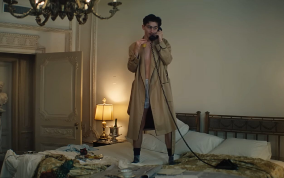 Timothy Chalamet is standing on a bed, in a robe, on the phone with someone, for his movie, "Marty Supreme"